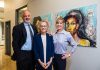 David, Sue, and Anna Kay Frueauff stand together next to a painting that incorporates gesture and text